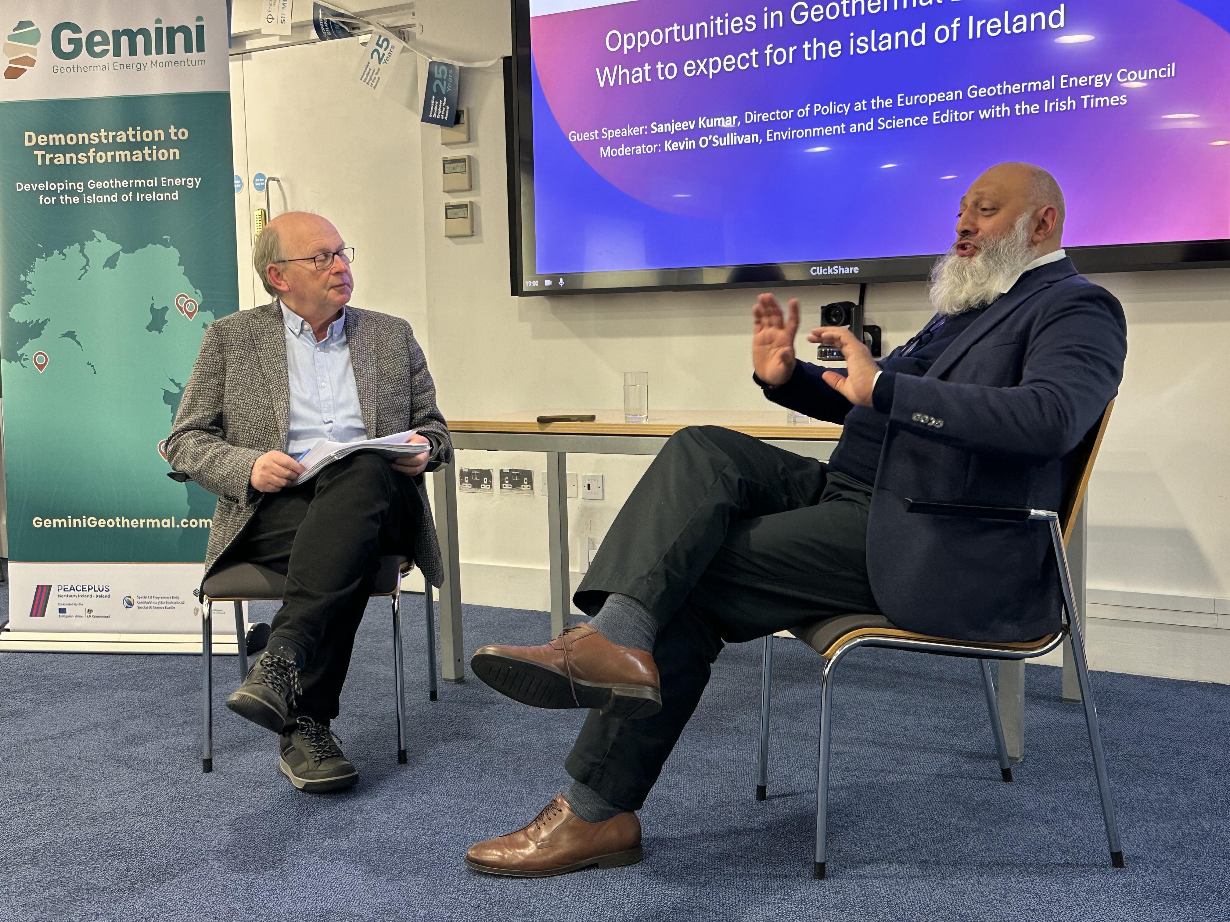Kevin O'Sullivan and Sanjeev Kumar seated at right-angles to each other and engaged in conversation. They are Indoors, with a pull up banner showing a partial map of the island of Ireland and the words GEMINI: Demonstration to Transformation and a screen showing the title of the evening's talk behind.